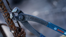 Metal pliers twisting wire around a rusty rebar at a construction site.