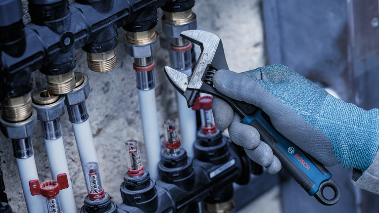 Person wearing safety equipment adjusts a pipe fitting with a wrench.