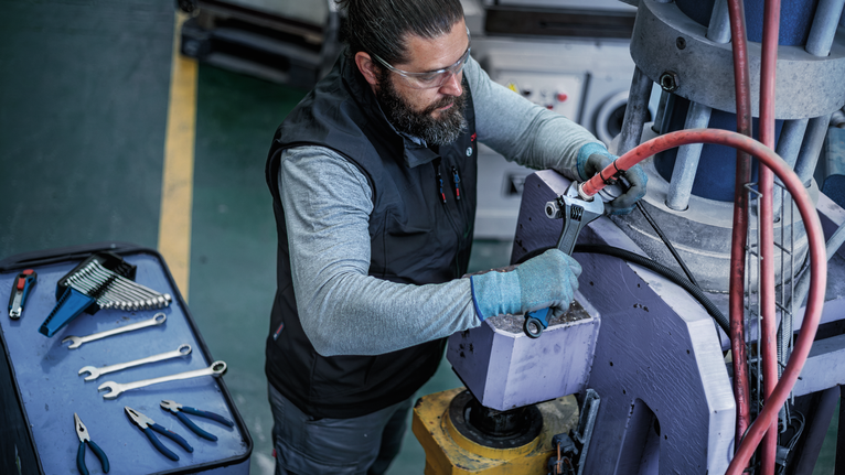 Person wearing safety equipment tightens a bolt on industrial machinery with a wrench.