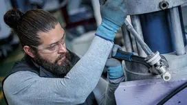 Person wearing safety equipment tightens a large metal pipe with a power wrench.