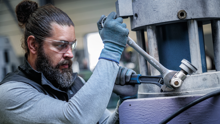 Person wearing safety equipment tightens a machine part with a wrench.