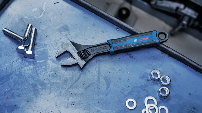Adjustable wrench lying on a workbench next to bolts, nuts, and washers.