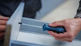 Person assembles a drawer using a blue and black screwdriver.