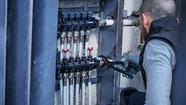 Person wearing safety equipment adjusts pipes with a wrench in a utility cabinet.