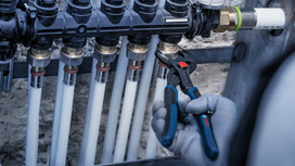 Person wearing safety equipment tightens a pipe fitting with pliers.