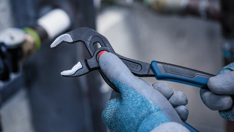 Person wearing safety equipment adjusts pliers near a metal pipe.