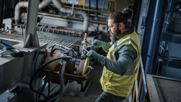 Person wearing safety equipment adjusts machinery in an industrial workshop.