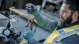 Person wearing safety equipment tightens a bolt on industrial machinery.