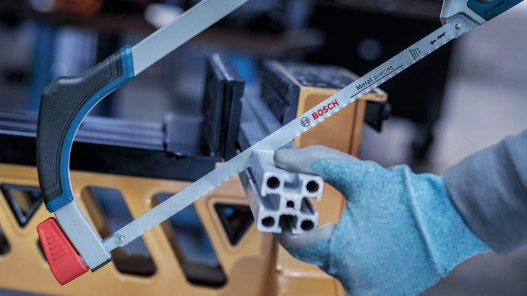 Person wearing safety equipment cuts metal tubing with a hand saw.