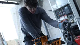 Person wearing safety equipment cuts metal with a table saw in a workshop.