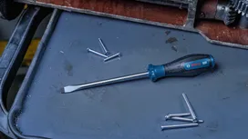 Flathead screwdriver on a workbench beside scattered metal screws.