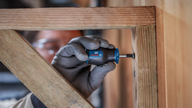 Person wearing safety equipment uses a screwdriver to fasten a screw in a wooden frame.