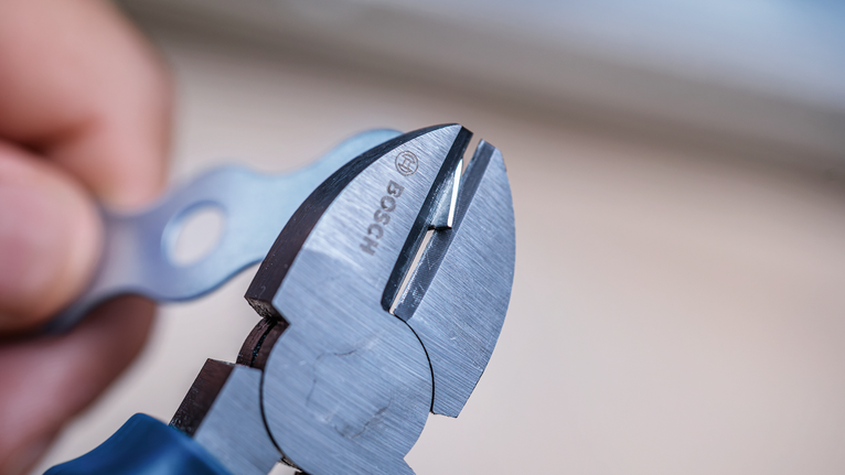 Person using diagonal pliers to cut a small metal wire.