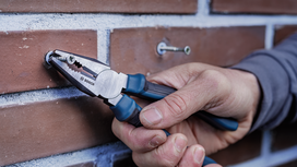 Person uses pliers to grip a screw inserted in a brick wall.