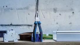 Pliers standing upright on a workbench beside electrical components and coiled cables.