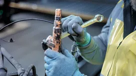 Person wearing safety equipment tightens a metal fitting with a wrench.