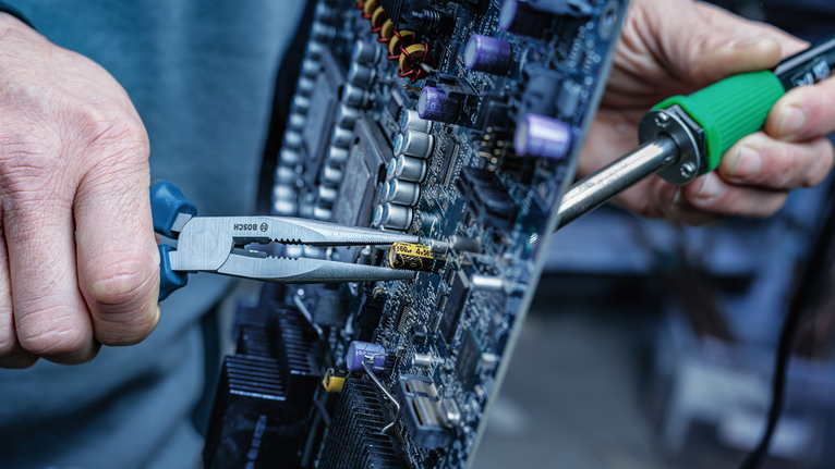 Person repairs a circuit board with pliers and a soldering iron.
