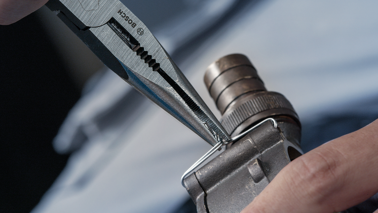 Person uses pliers to bend a metal wire on a mechanical part.