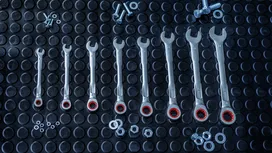 A set of seven combination wrenches arranged by size on a textured black rubber mat.