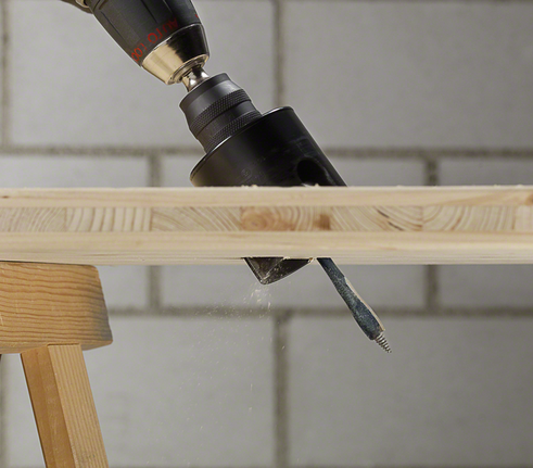 Perceuse avec un accessoire de scie cloche perçant une planche de bois.