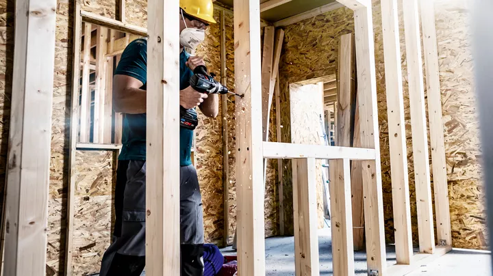 Une personne portant un équipement de sécurité perce un cadre en bois sur un chantier de construction.
