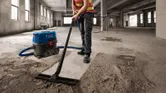 Une personne portant un équipement de sécurité aspire la poussière de béton dans un grand bâtiment inachevé.