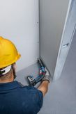 Une personne portant un équipement de sécurité fixe des cloisons sèches à l’aide d’un tournevis sans fil.