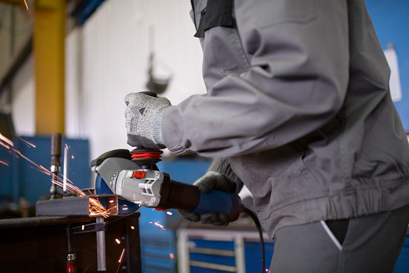 Une personne portant un équipement de sécurité meule du métal, produisant des étincelles dans un atelier.