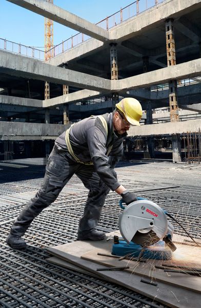 Une personne portant un équipement de sécurité coupe des tuyaux métalliques sur un chantier de construction avec une tronçonneuse.
