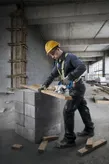 Une personne portant un équipement de sécurité coupe du bois avec une scie circulaire sur des blocs de béton.