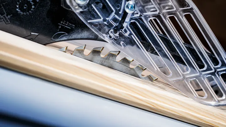 Lame de scie circulaire coupant une planche de bois avec un protège-lame en plastique.