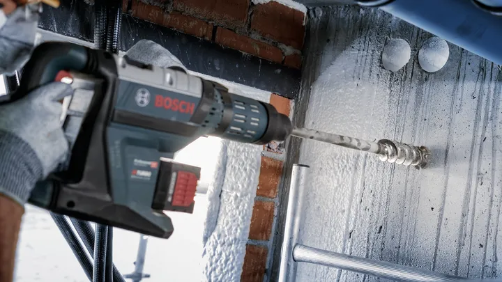 Une personne portant un équipement de sécurité perce un plafond en béton.