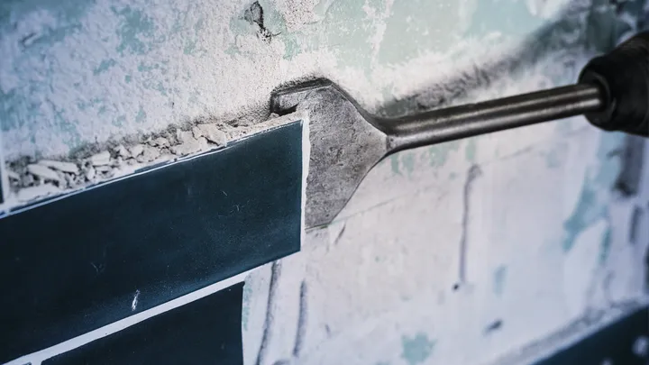 Outil de ciseau retirant des carreaux de céramique d'une surface murale poussiéreuse.