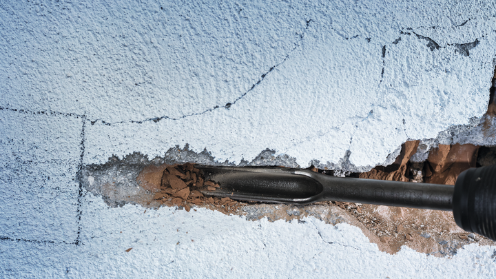 Ciseau démolissant un mur de béton fissuré.