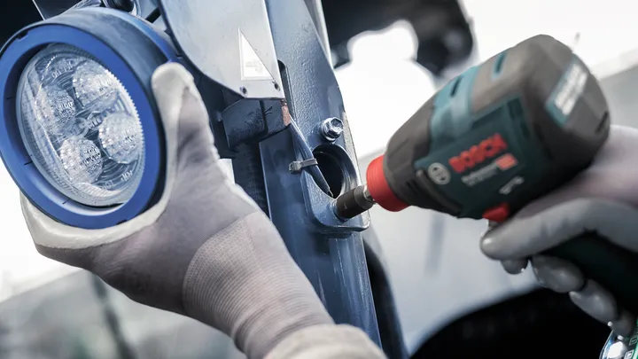 Une personne portant un équipement de sécurité utilise un outil électrique pour fixer un support métallique près d'une lumière.