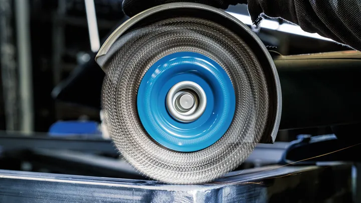 Une personne portant un équipement de sécurité broie du métal avec une meule abrasive rotative.