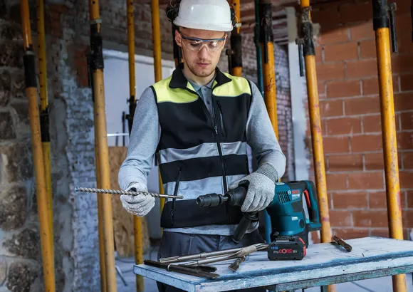 Une personne portant un équipement de sécurité fixe un foret à un outil électrique sur un chantier de construction.