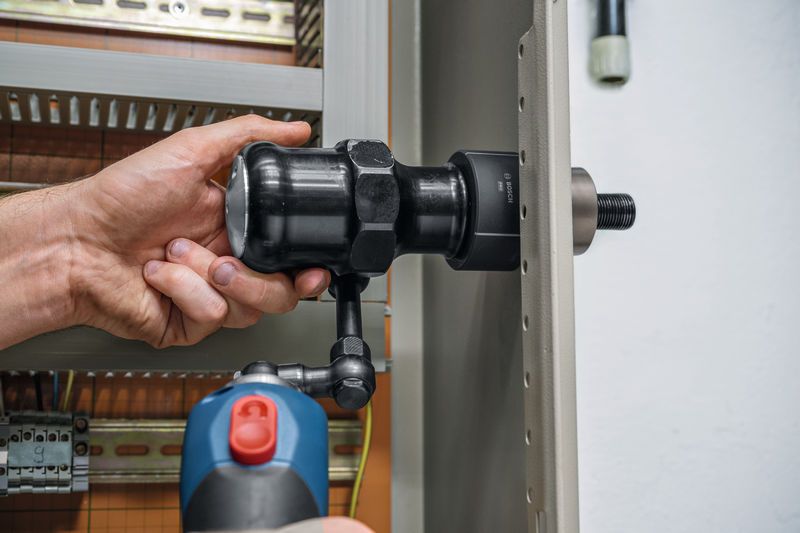 Une personne utilise un outil de poinçonnage hydraulique sans fil sur un panneau métallique.