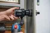 Une personne utilise un outil de poinçonnage hydraulique sans fil sur un panneau métallique.