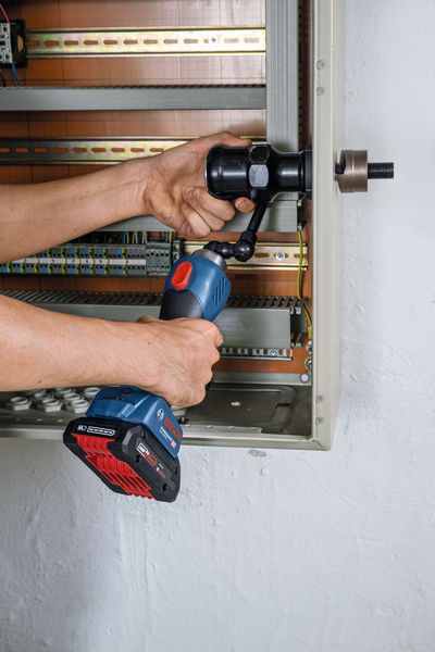 Une personne utilise un outil de poinçonnage hydraulique sans fil pour percer un trou dans un panneau électrique.