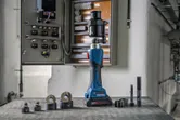 Outil de poinçonnage hydraulique sans fil avec divers accessoires placés à proximité d'un panneau de commande ouvert.