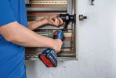 Une personne utilise un outil de poinçonnage hydraulique sans fil sur un panneau électrique.