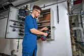 Une personne portant un équipement de sécurité perce un trou dans une armoire électrique à l'aide d'un outil sans fil.