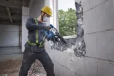 Un ouvrier portant un équipement de sécurité utilise un marteau de démolition pour briser un mur carrelé.