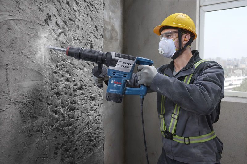 Une personne portant un équipement de sécurité utilise un marteau de démolition pour briser un mur en béton.
