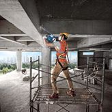 Une personne portant un équipement de sécurité utilise un marteau de démolition sur une poutre en béton.