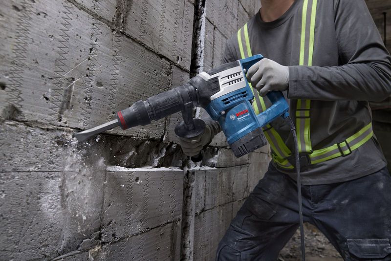 Une personne portant un équipement de sécurité utilise un marteau de démolition pour briser un mur en béton.