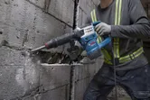Une personne portant un équipement de sécurité utilise un marteau de démolition pour briser un mur en béton.