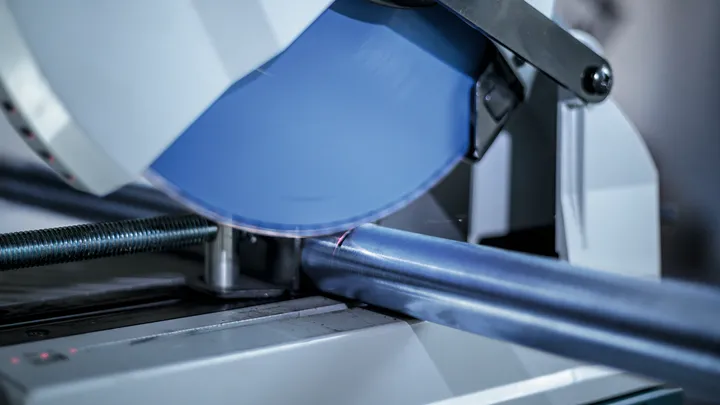 Tube métallique coupé par une scie circulaire dans un atelier.