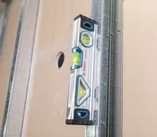 Niveau à bulle aligné contre un panneau de plaques de plâtre comportant une découpe.